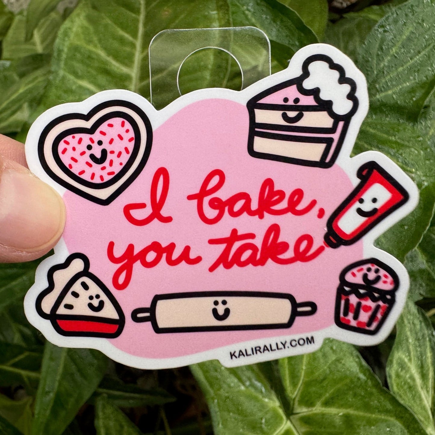 This cute baking sticker features a cookie, piece of cake, piece of pie, a rolling pin, some frosting in a tube, and a a cupcake, all smiling, with the words, "I bake you take." Colors are pink, red, black and white.