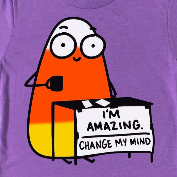 Purple Candy Corn t-shirt zoomed in, with a cartoon candy corn character with a sign saying 'I'm Amazing. Change My Mind'