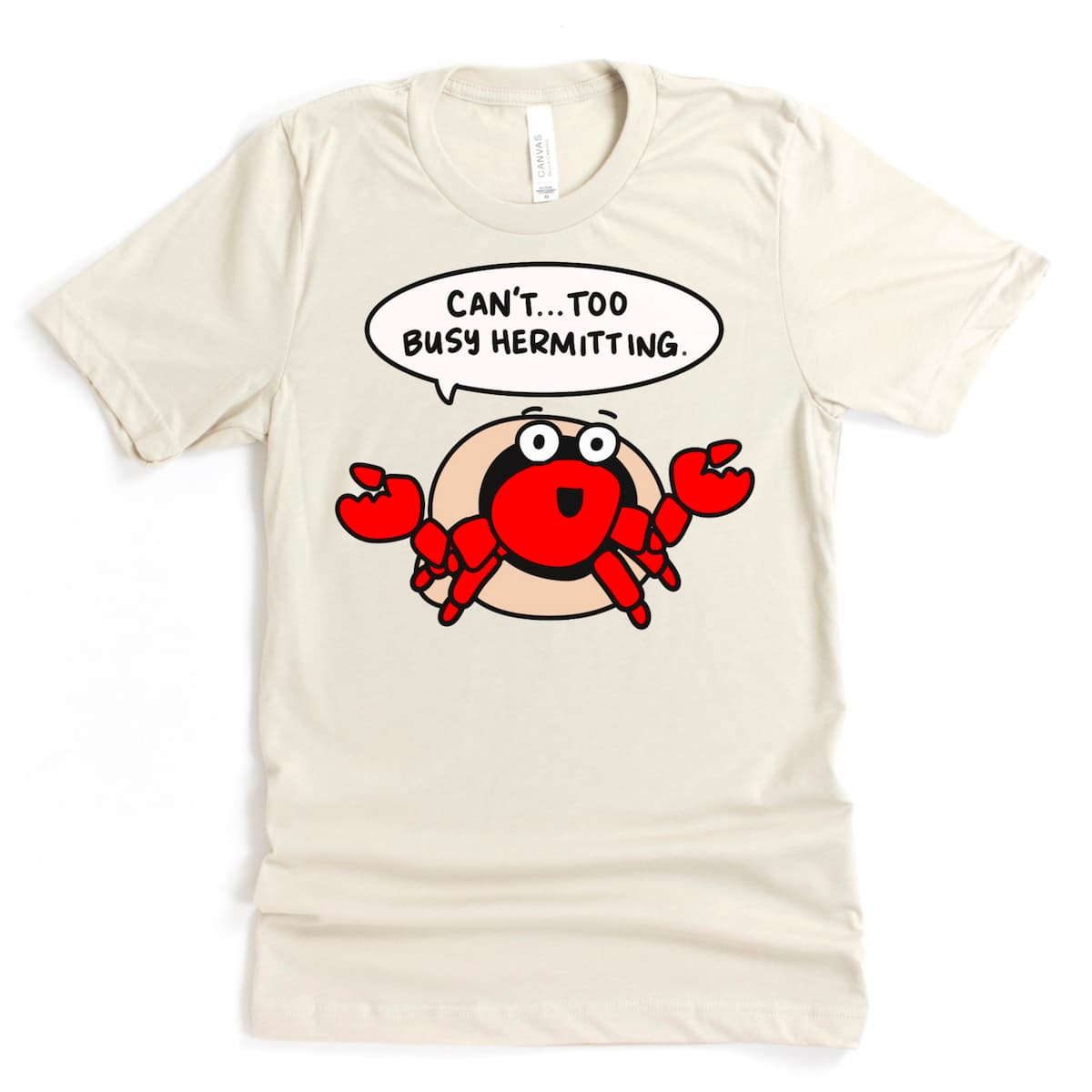 Flat lay of a Heather Dust Colored Beach Tee Shirt - “Can't. Too Busy Hermitting.” t-shirt by Kalirally, featuring a cartoon hermit crab design for introverts.