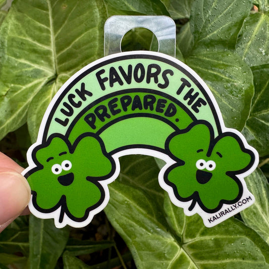 Cartoon shamrock and rainbow sticker with phrase “Luck favors the prepared” by Kalirally