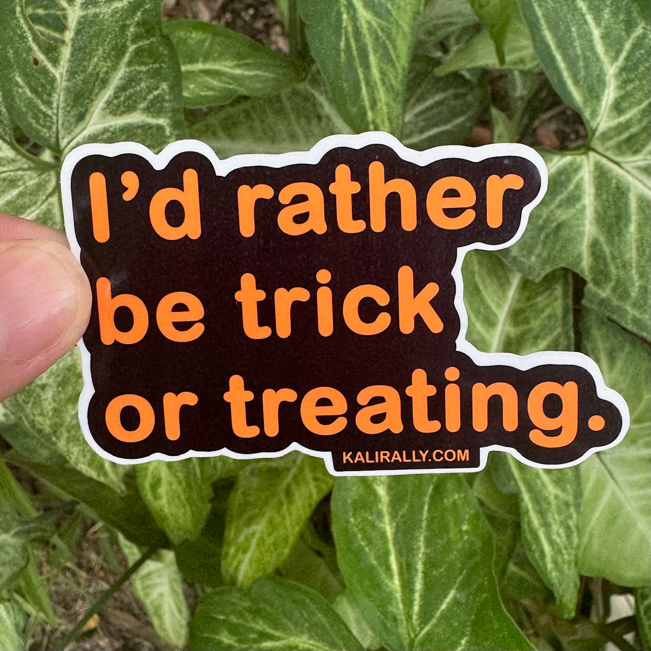 Text-only Halloween sticker with bold orange lettering on a black background that reads “I’d rather be trick or treating,” durable and waterproof by Kalirally.