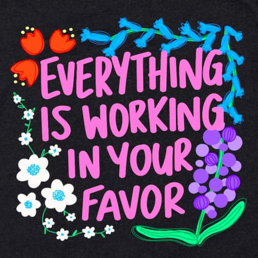 Close-up of positive affirmation graphic tee showing “Everything is working in your favor” phrase in Heather Black by Kalirally