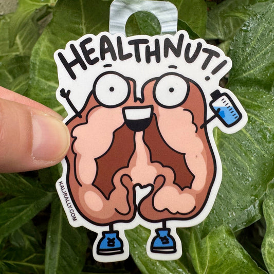 Walnut cartoon character sticker labeled 'HEALTHNUT!' with water bottle and gym shoes, held in front of green leaves