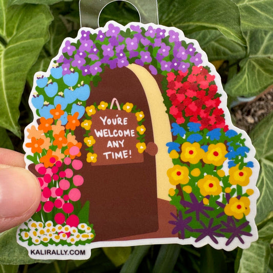 Open Door Sticker with cartoon door, flowers, and phrase “You're welcome here any time!”, welcoming decal by Kalirally