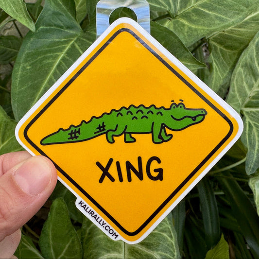 Cute thinking about you sticker with cartoon alligator sitting on a rainbow saying “Just over here thinkin’ about ya.” Long-distance friendship vinyl decal.