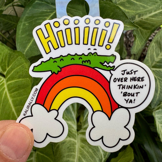 Cute thinking about you sticker with cartoon alligator sitting on a rainbow saying “Just over here thinkin’ about ya.” Long-distance friendship vinyl decal.